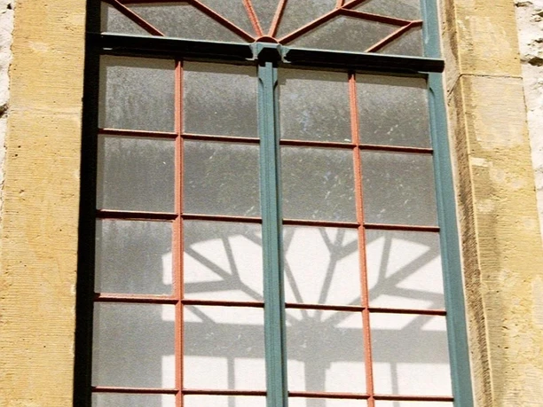 Fenster einer Synagoge mit geschwungenen Eisenverzierungen im oberen Bereich, Holzrahmen in Sandstein.