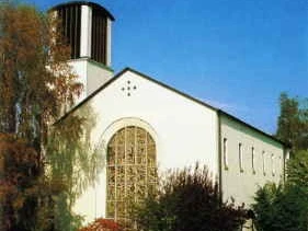 Die katholische Kirche St. Michael mit markantem Turm thront umgeben von Bäumen unter blauem Himmel.