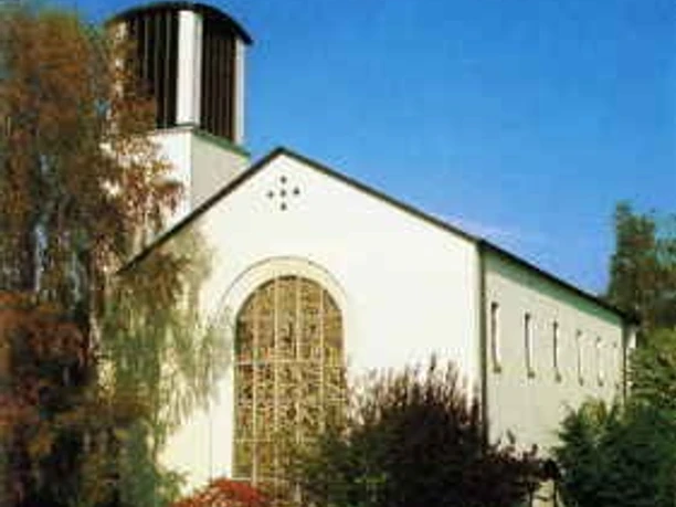 Die katholische Kirche St. Michael mit markantem Turm thront umgeben von Bäumen unter blauem Himmel.