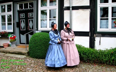Stiftsdamen begleiten die historische Erlebnisführung Zwei Frauen in traditioneller Kleidung stehen vor einem historischen Gebäude auf gepflastertem Boden.