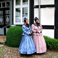 Stiftsdamen begleiten die historische Erlebnisführung Zwei Frauen in traditioneller Kleidung stehen vor einem historischen Gebäude auf gepflastertem Boden.