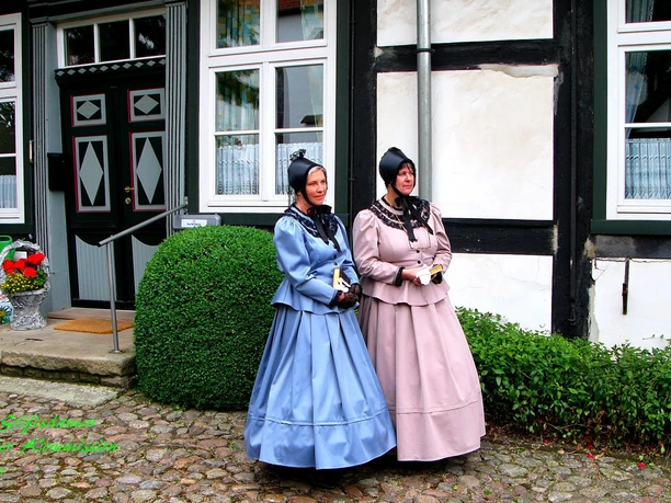 Stiftsdamen begleiten die historische Erlebnisführung Zwei Frauen in traditioneller Kleidung stehen vor einem historischen Gebäude auf gepflastertem Boden.