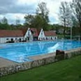 Freibad Schlangen Becken mit Gebäuden Großes Freibadbecken mit blauem Wasser, flankiert von weißen Gebäuden und umgeben von Bäumen.