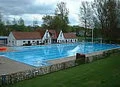 Freibad Schlangen Becken mit Gebäuden Großes Freibadbecken mit blauem Wasser, flankiert von weißen Gebäuden und umgeben von Bäumen.