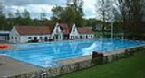 Freibad Schlangen Becken mit Gebäuden Großes Freibadbecken mit blauem Wasser, flankiert von weißen Gebäuden und umgeben von Bäumen.