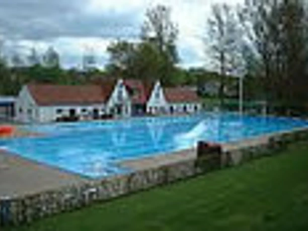 Freibad Schlangen Becken mit Gebäuden Großes Freibadbecken mit blauem Wasser, flankiert von weißen Gebäuden und umgeben von Bäumen.
