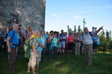 Wandergruppe am Aussichtsturm Eine Wandergruppe steht neben einem steinernen Aussichtsturm und hört einem Guide zu, der in die Ferne zeigt.