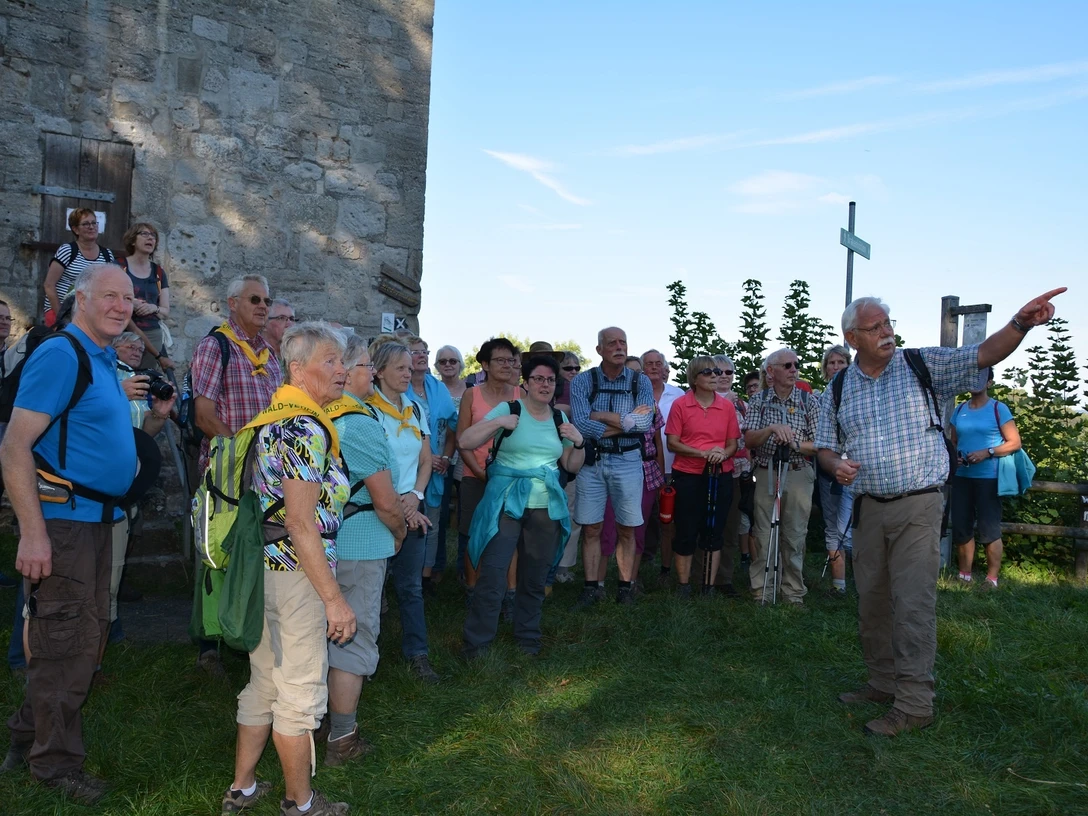 Wandergruppe am Aussichtsturm Eine Wandergruppe steht neben einem steinernen Aussichtsturm und hört einem Guide zu, der in die Ferne zeigt.