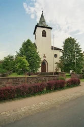 kath. Kirche in Amelunxen Katholische Kirche Amelunxen mit weißem Turm und grünem Dach, flankiert von Bäumen und Büschen.