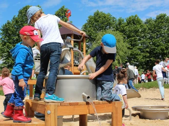 Kinder spielen an einem Wasserspielplatz mit Sand und Kletterelementen unter freiem Himmel.