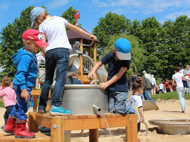 Kinder spielen an einem Wasserspielplatz mit Sand und Kletterelementen unter freiem Himmel.