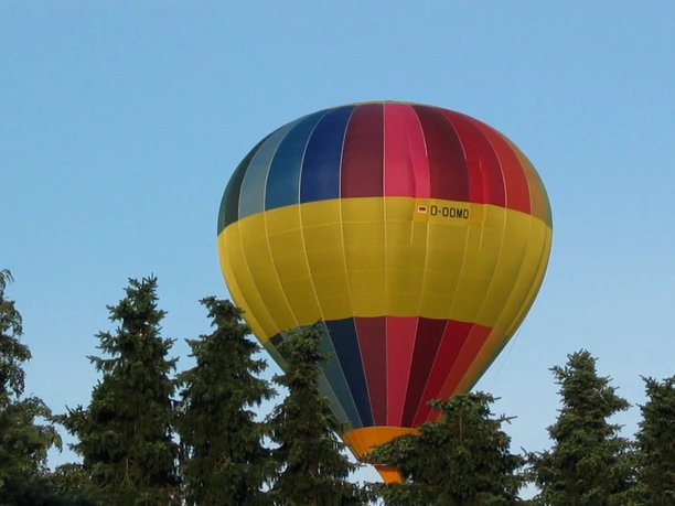 Segelflugplatz Ballon Heißluftballon mit farbenfrohen Streifen schwebt über dichten Nadelbäumen bei klarem Himmel.