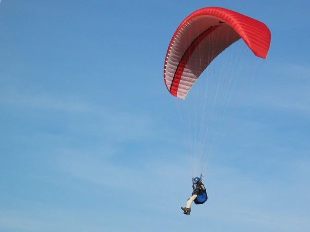 Segelflugplatz Gleitschirmflieder Gleitschirmflieger schwebt mit rotem Schirm über blauem Himmel, sanfte Bewegung in luftiger Höhe.