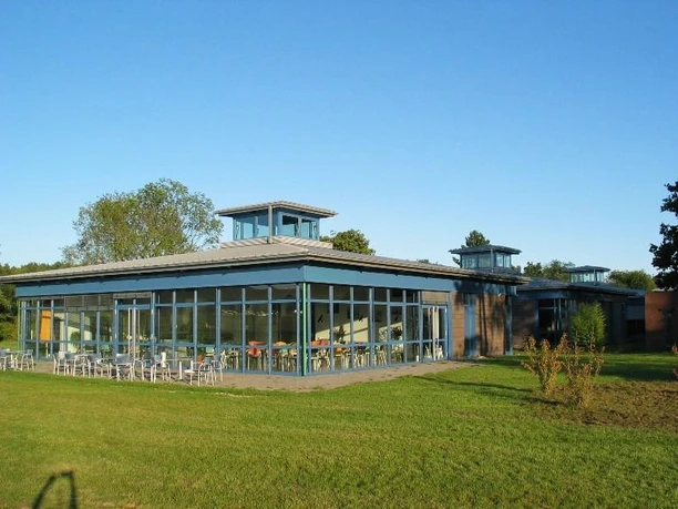 Segelflugschule Moderne Segelflugschule mit großen Glasfronten, umgeben von Grünflächen und klarem Himmel.