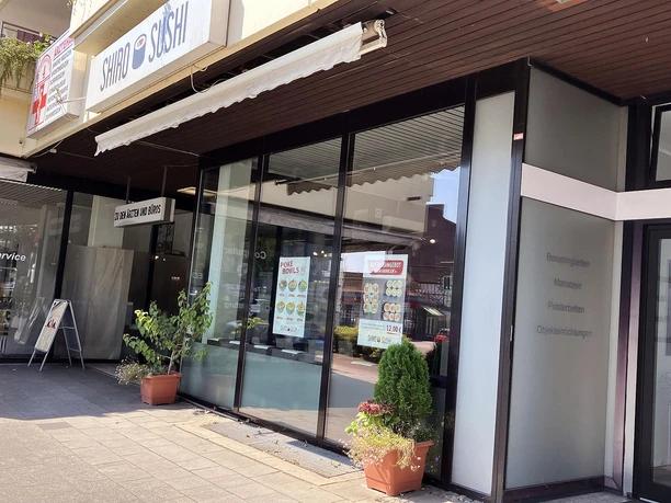 Eingang von Shiro Sushi mit Schaufenstern, Speisekarten und Pflanzkübeln vor dem Lokal