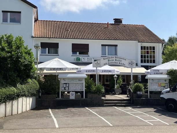 Restaurant Beim Ritter mit Biergarten, Sonnenschirmen und Parkplatz vor hellem Gebäude