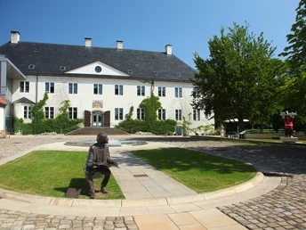 Schloss Benkhausen Schloss Benkhausen mit gepflegter Gartenanlage und Skulptur auf gepflastertem Vorplatz im Sonnenschein.