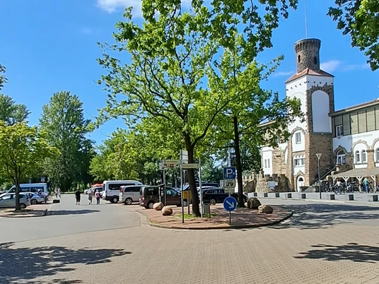 Parkplatz Strandterrassen Parkplatz in Strandnähe mit Schatten spendenden Bäumen und einem historischen Turm im Hintergrund.