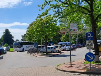 Parkplatz Strandterrassen mit Busparkplatz Parkplatz mit gekennzeichneten Flächen für Busse und Fahrräder, umgeben von grünen Bäumen.