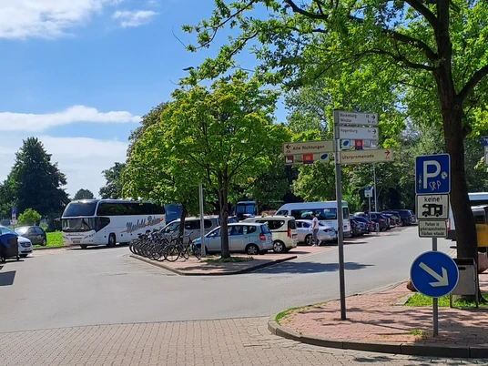 Parkplatz Strandterrassen mit Busparkplatz Parkplatz mit gekennzeichneten Flächen für Busse und Fahrräder, umgeben von grünen Bäumen.