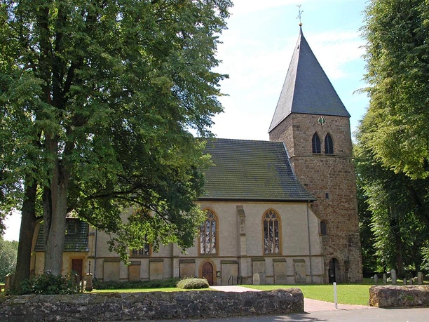 Stiftskirche in Stift Quernheim mit steinernem Glockenturm und umgebenden Laubbäumen im Sommer.