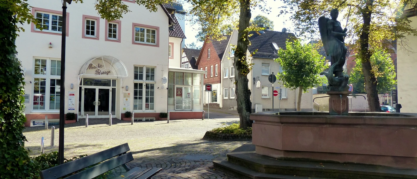 Service-Center + Brunnen Ein historisches Haus mit Fachwerk an einem gepflasterten Platz, umgeben von Bäumen und einem Brunnen.