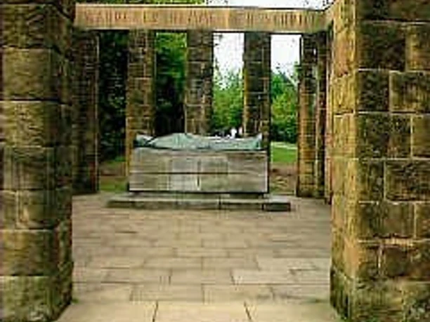 Ehrenmal Steinernes Ehrenmal mit Säulen, zentralem Sarkophag und umliegenden Bäumen im Hintergrund.