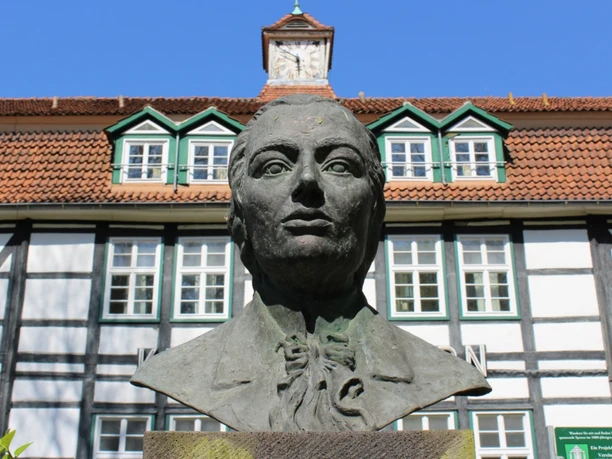Dr. Trampel-Büste vor historischem Fachwerkhaus im Kurpark von Bad Meinberg