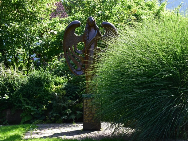 Engelsstatue im Lebensgarten Amelunxen Bronzefarbene Engelsstatue neben Gräsern im Lebensgarten Amelunxen