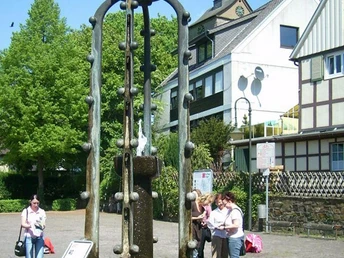 Wasser sprudelt aus einem kunstvollen Brunnen mit Widukind-Reiterfigur; umgeben von Fachwerkhäusern.