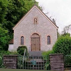 Antoniuskapelle Steinerne Kapelle mit Stufen, Holzportal und kleinen Fenstern, umgeben von grüner Vegetation.