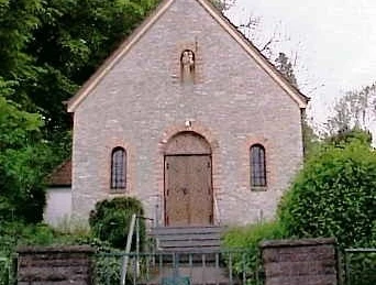 Antoniuskapelle Steinerne Kapelle mit Stufen, Holzportal und kleinen Fenstern, umgeben von grüner Vegetation.