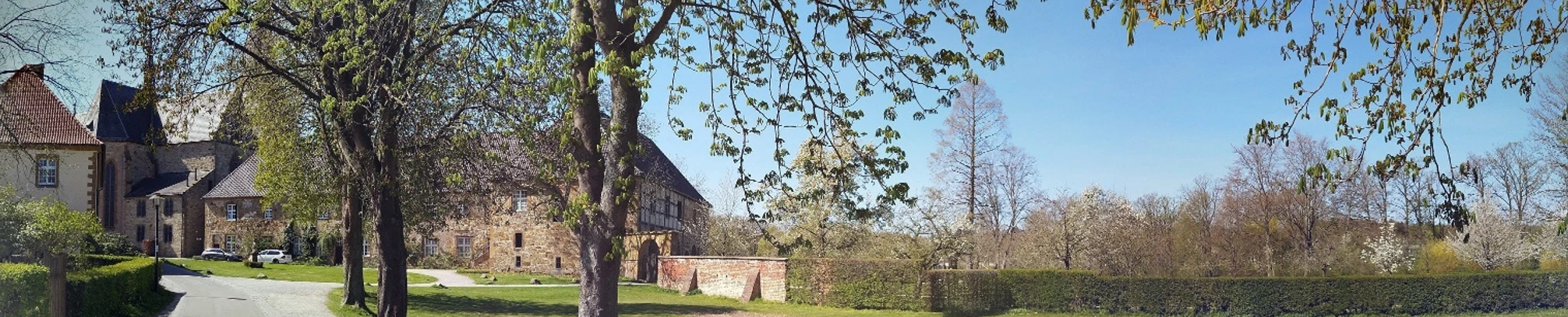 Burganlage mit historischen Gebäuden und gepflegter Gartenanlagen, umgeben von grünen Bäumen.