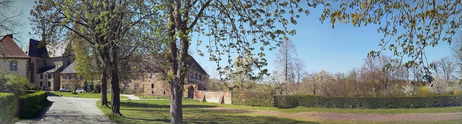Kloster Herzebrock Burganlage mit historischen Gebäuden und gepflegter Gartenanlagen, umgeben von grünen Bäumen.