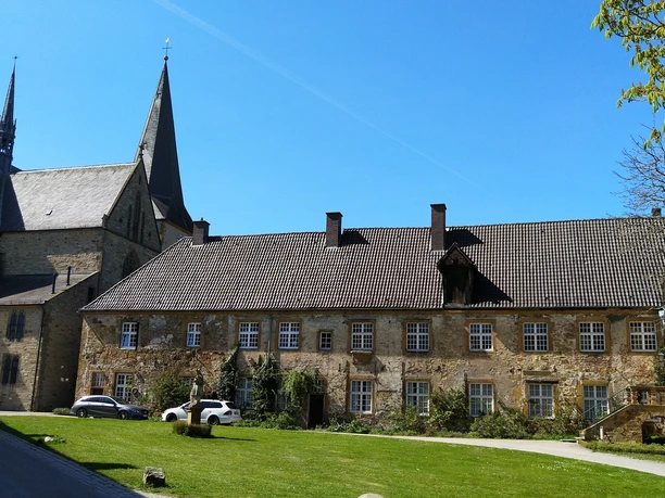 Klosteranlage mit historischen Gebäuden, spitzen Kirchtürmen und gepflegter Rasenfläche im Vordergrund.