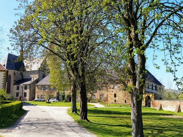 Kloster Herzebrock Historische Schlossanlage mit gepflastertem Weg, umgeben von grünen Bäumen und Rasenflächen.
