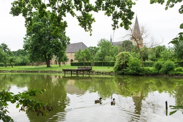 Teich im Garten der Klosteranlage Herzebrock Ruhiger Teich mit Enten im Vordergrund, alte Kirche und gepflegte Gärten im Hintergrund.
