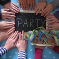 Kinderhände umrahmen eine Tafel mit buntgeschriebenem "PARTY", neben Luftschlangen.