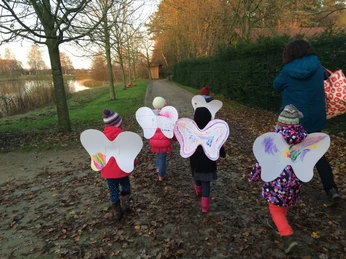 Im Zauberreich der Feen und Elfen Kinder in bunten Herbstoutfits mit selbstgebastelten Flügeln laufen fröhlich einen Waldweg entlang.