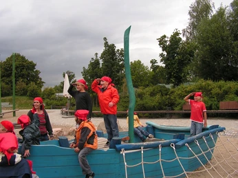 Piratenfest Kinder in Piratenkostümen spielen auf einem hölzernen Spielplatzschiff, umgeben von grüner Natur.