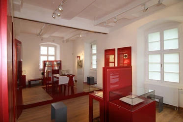 Ausstellung Altes Gericht Fürstenberg Innenraum einer historischen Ausstellung mit roten Infotafeln und Ausstellungsstücken in Glasvitrinen.