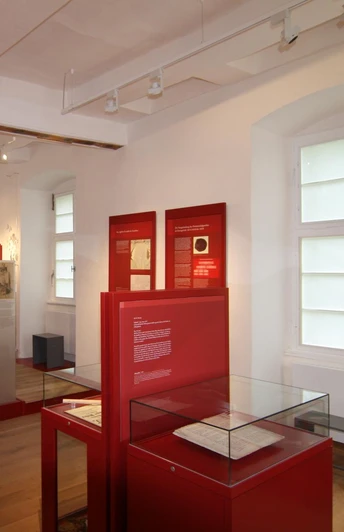 Ausstellung Altes Gericht Fürstenberg Innenraum einer historischen Ausstellung mit roten Infotafeln und Ausstellungsstücken in Glasvitrinen.
