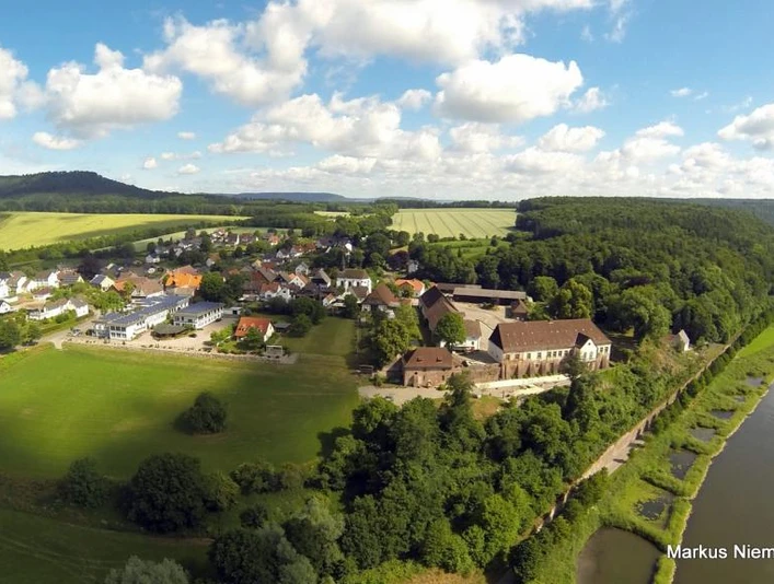 Blankenau im Weserbergland Die Luftaufnahme zeigt den Ort Blankenau. Rechts im Bild fließt die Weser, im Hintergrund sind Felder, Wiesen und Bäume zu sehen.