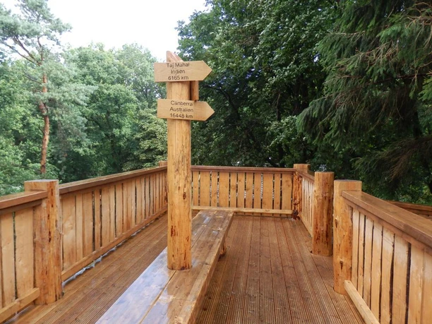 Holzplattform mit Richtungsschildern vor Waldkulisse, lädt zur Aussicht und Orientierung ein.