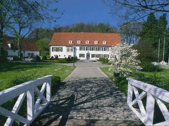 Historische Villa mit roten Dachziegeln, umgeben von gepflegtem Garten und einer schönen Steinbrücke.