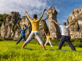 Vier Personen machen Yoga vor den beeindruckenden Felsformationen der Externsteine im Grünen.