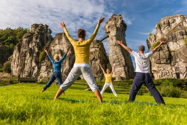 externsteine-horn-bad-meinberg-322-teutoburgerwaldtourismus-dominik-ketz Vier Personen machen Yoga vor den beeindruckenden Felsformationen der Externsteine im Grünen.