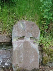 Der Kreuzstein Grauer Bundsandsteinblock mit einem steinernen Kreuz, umgeben von Gras