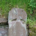 Der Kreuzstein Grauer Bundsandsteinblock mit einem steinernen Kreuz, umgeben von Gras