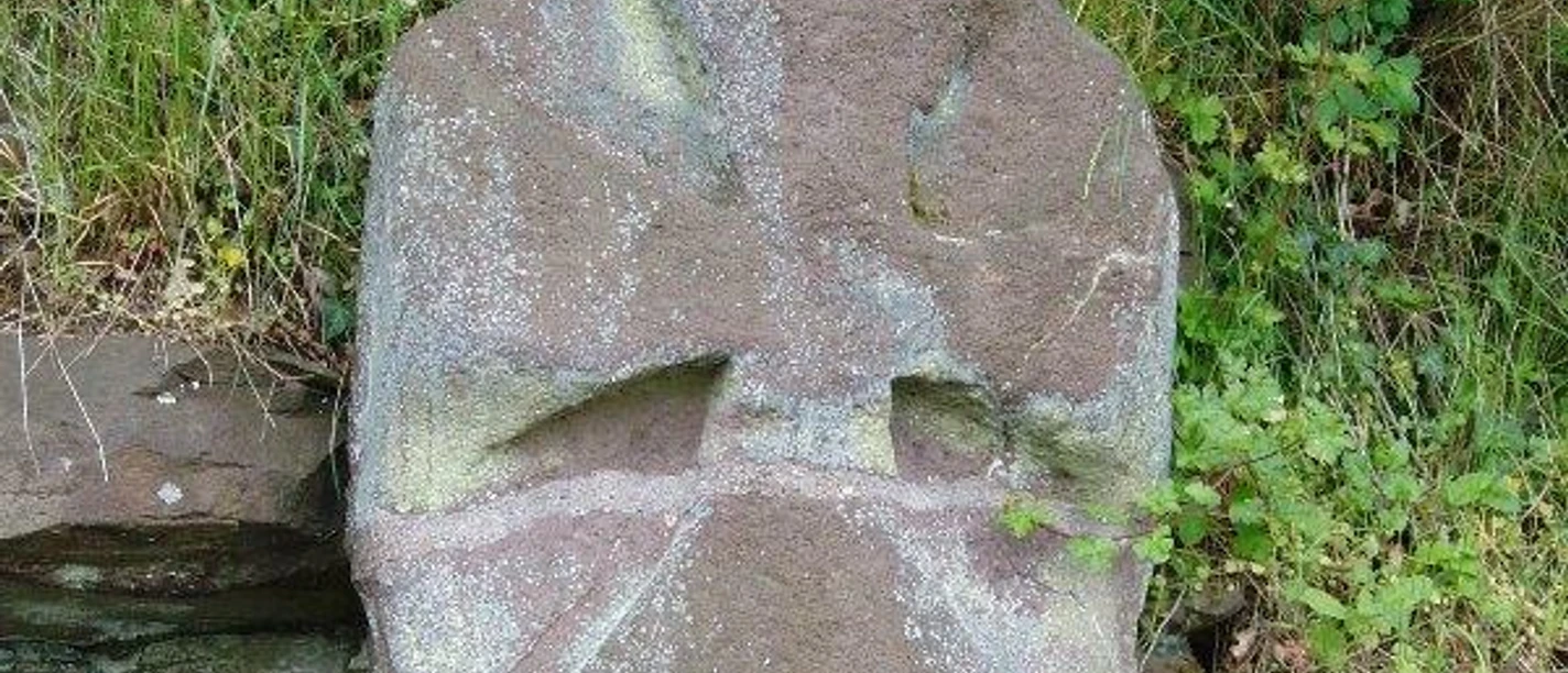 Der Kreuzstein Grauer Bundsandsteinblock mit einem steinernen Kreuz, umgeben von Gras